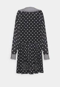 Robe noire à pois avec tissu transparent, manches longues, col vichy et accents de perles sur les poignets. Design plissé en bas.