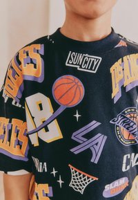 Basketbollstema t-shirt med svart bakgrund som har ljusa lila, gula och vita grafik, inklusive logotyper och basketbollar.