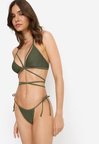 Σετ μαγιό πράσινο με τριγωνικό τοπ με λουριά που διασταυρώνονται και μπικίνι χαμηλόμεσο με ρυθμιζόμενους δεσίμους, κατασκευασμένο από ελαστικό ύφασμα.
