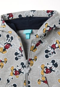 Sweat à fermeture éclair gris avec un motif répété de Mickey Mouse en rouge, noir et jaune. Accentué par un zip gris en forme de Mickey.