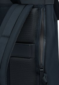 Donkerblauwe rugzak met gestructureerd gaas en gladde stofsecties, verstelbare gewatteerde schouderbanden en een zijrits.