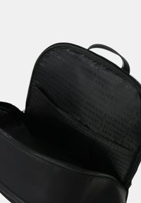 Bolsita de cuero negro con cremallera abierta para mostrar el forro interior con un patrón de texto repetido de "Armani Exchange" y un bolsillo interior.