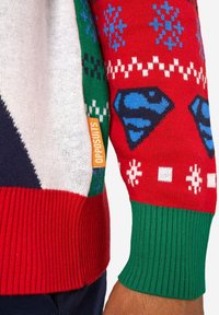 Farebný sveter s kombináciou červenej, zelenej a bielej farby. Obsahuje geometrické vzory, vločky a logá Supermana. Má rebrované manžety a lem.