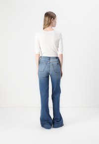 Pull en crème léger à manches trois-quarts associé à un jean en denim bleu taille haute évasé avec deux poches arrière.