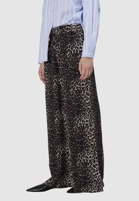 Luipaardprint, wijde broek in zwart en bruin stof, met een zachte textuur en een elastische tailleband, gecombineerd met een lichtblauw gestreept shirt.