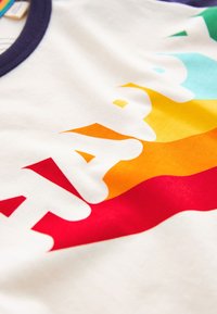 Bela bombažna majica z večbarvnim napisom "SREČNO" v prelivajočih odtenkih rdeče, oranžne, rumene in turkizne na teksturirani tkanini.