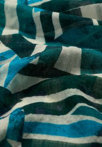 Tessuto con una consistenza leggera e semitrasparente caratterizzato da audaci strisce color teal, verde e bianco di larghezze variabili.