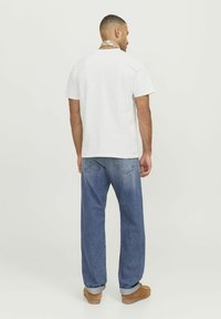 White short-sleeve t-shirt with a relaxed fit, paired with faded blue denim jeans and brown shoes, featuring rolled cuffs and back pockets.