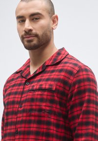 Czerwona i czarna flanelowa koszula w kratę z zapinanym na guziki przodem, kołnierzykiem i pojedynczą kieszenią na piersi, charakteryzująca się miękką fakturą i dopasowanym krojem.