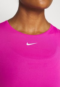Přiléhavý růžový sportovní top s krátkými rukávy, vyrobený z texturované, prodyšné tkaniny. Na přední straně se nachází bílé logo Nike swoosh.