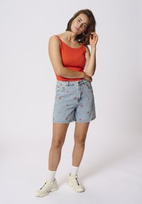 Punase sobran t-särk, heledad sinised denim-lühikesed püksid lillekirjaga ja valged tennised. Püksid on klassikalise lõikega ja kõrge vöökohaga.
