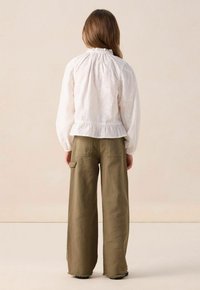White embroidered blouse with a ruffled neckline and long sleeves, paired with olive green wide-leg trousers featuring side pockets.