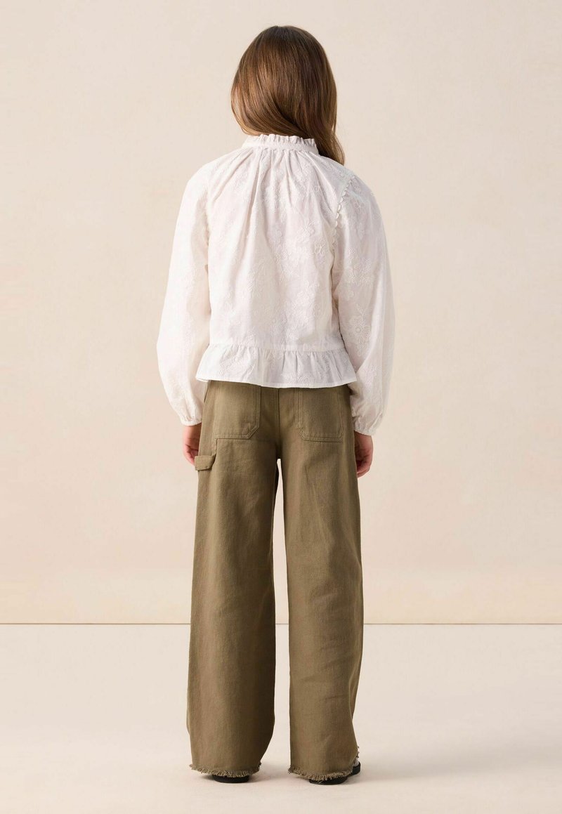 White embroidered blouse with a ruffled neckline and long sleeves, paired with olive green wide-leg trousers featuring side pockets.