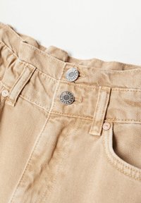 Pantalon en denim beige avec deux boutons argentés, passants de ceinture et couture détaillée autour de la taille et du bord de la poche avant.
