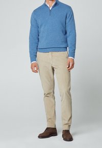 Ljusblå stickad tröja med kvartslång dragkedja, khaki smala byxor och bruna mockaskor. Slät textur och avslappnad passform.