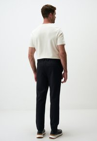 Kurzärmliges cremefarbenes Hemd kombiniert mit schwarzen Hosen, die über einen elastischen Bund und Seitentaschen verfügen, getragen mit schwarzen Sneakers.