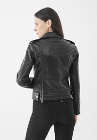 Giubbotto da motociclista in pelle nera con un design aderente, tasche con cerniera, spalline e una texture liscia. Cerniere decorative sui polsini.