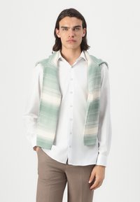 Gilet tricoté vert clair à motif avec des rayures crème, porté par-dessus une chemise blanche. Il présente une capuche et un design à l'avant ouvert. Ajustement ajusté, style décontracté.