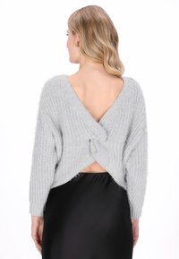 Grijze, fluffy gebreide trui met lange mouwen en een diepe V-rugdetail, met een verweven rugontwerp, gecombineerd met een zwarte satijnen rok.