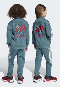 Teal urheiluasu, jossa on Spiderman-kuvio takana, valkoiset sivusuunnittelut housuissa ja musta-punaiset lenkkarit verkkosuunnittelulla.