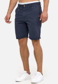 Shorts en coton bleu marine avec ourlets repliés, poches avant et arrière, fermeture par bouton et fermeture éclair, et une petite étiquette de marque sur la poche gauche.
