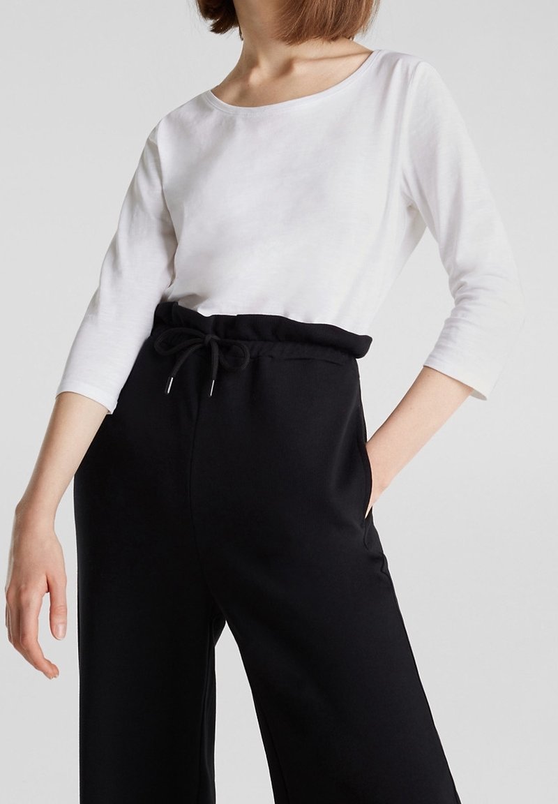 Witte lange mouwen top met een ronde hals, gecombineerd met hoge zwarte sweatpants met een trekkoord en zijzakken.