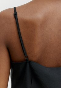 Schwarzes Camisole mit dünnen Trägern und verstellbaren Details, das eine glatte Textur und eine figurnahe Passform aufweist, von hinten dargestellt.