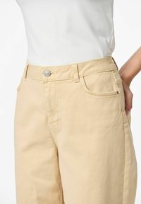Pantalons taille haute beige clair en tissu mélange de coton. Comprend un bouton argenté, des poches avant et une coupe droite.