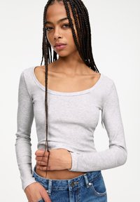 Ljusgrå långärmad ribbad tröja med rundad halsringning, figurnära design och mjuk textur, matchad med blå högmidjade jeans.