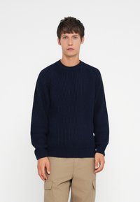 Navy blue knitted sweater with a ribbed texture, round neck, and long sleeves, paired with khaki cargo pants. Simple, casual design.