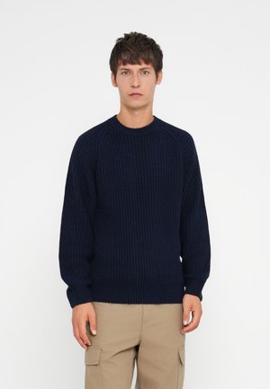 Navy blue knitted sweater with a ribbed texture, round neck, and long sleeves, paired with khaki cargo pants. Simple, casual design.