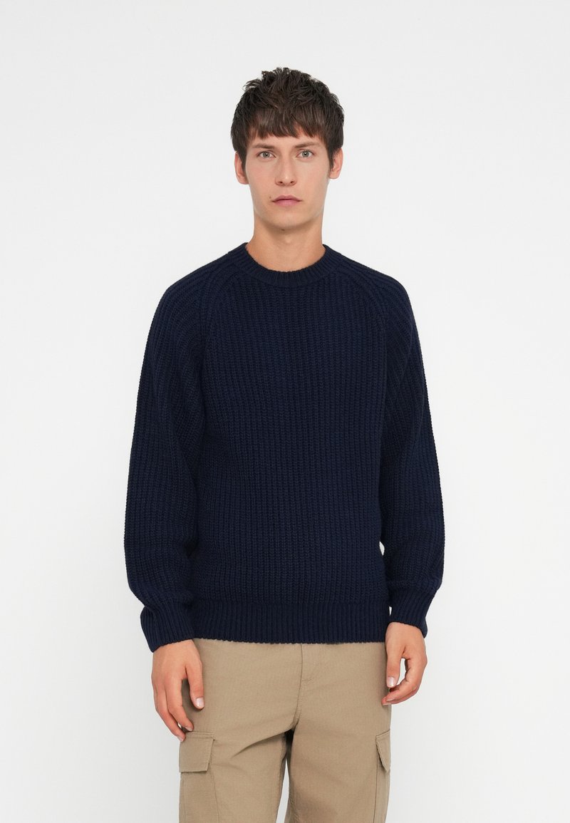 Navy blue knitted sweater with a ribbed texture, round neck, and long sleeves, paired with khaki cargo pants. Simple, casual design.
