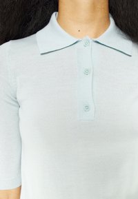 Světle modrá polo košile s krátkým rukávem vyrobená z pletené látky, se límečkem, pěti knoflíky a hladkým povrchem.