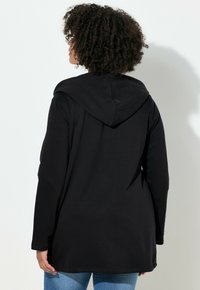 Felpa nera a maniche lunghe con cappuccio, orlo arrotondato e coulisse regolabile. Tessuto liscio e vestibilità comoda, abbinata a jeans azzurri.