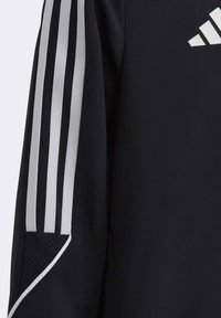 Zwarte sportjack met drie witte verticale strepen op de mouwen. Bevat een textuuraccent op de mouw en een logodetail.