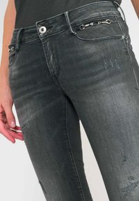 Grijze denim jeans hebben een aansluitend ontwerp met versleten details, een gladde textuur en een decoratieve zilveren kettingaccent bij de zak.