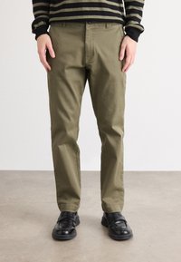 Chino verde măsliniu din material durabil, cu un croi clasic drept și un design subtil al buzunarelor frontale. Asortați cu pantofi negri.