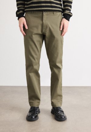 Olive green chinos made of durable fabric, featuring a classic straight-leg cut and subtle front pocket design. Paired with black shoes.