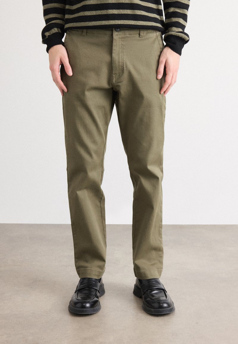 Chino verde măsliniu din material durabil, cu un croi clasic drept și un design subtil al buzunarelor frontale. Asortați cu pantofi negri.