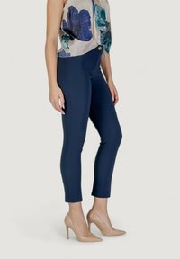 Pantaloni fitted blu navy con una texture liscia, vita alta e una silhouette pulita, abbinati a scarpe con tacco nude.