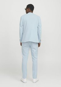 Helles blaues Sakko mit einer taillierten Passform, ausgestattet mit einem einzelnen Schlitz hinten, kombiniert mit weißen Sneakers. Einfaches monochromes Design.