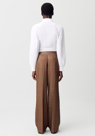 Blusa blanca de manga larga con un diseño recortado. Pantalones anchos de patrón marrón con un estampado geométrico y una cinturilla de contraste.