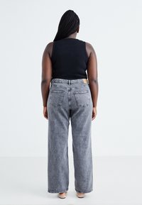 Rear view of a person wearing high-waisted, wide-leg black jeans with a textured finish and two back pockets. Paired with a black tank top.