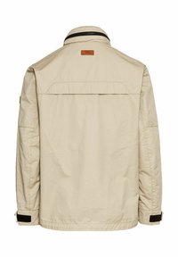 Beżowa, lekka kurtka z kołnierzykiem, detalem w okolicy pleców i czarnym akcentem przy mankietach. Tkana tkanina oraz skórzana naszywka z logo na karku.