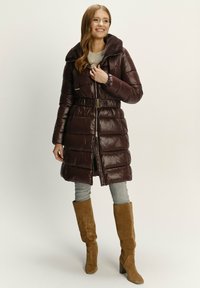 Hnědý zateplený kabát s kožíškovým límcem, páskem v oblasti pasu a zipovým zapínáním. Nosit se se šedými džíny a hnědými semišovými vysokými botami.