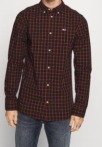 Schwarz-rot kariertes Hemd mit Knopfkragen, langen Ärmeln und Logo-Akzent auf der Brust. Hergestellt aus leichtem Stoff.