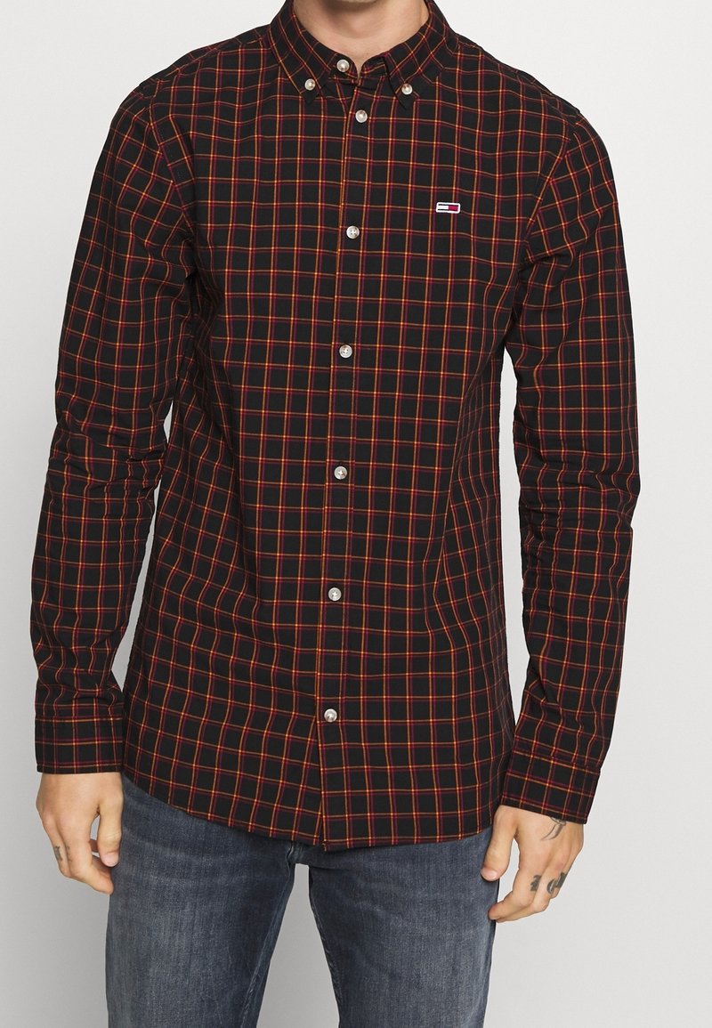 Schwarz-rot kariertes Hemd mit Knopfkragen, langen Ärmeln und Logo-Akzent auf der Brust. Hergestellt aus leichtem Stoff.