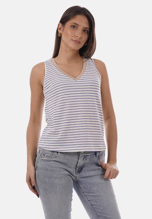 Giovane donna con top bianco senza maniche a scollo a V con sottili strisce blu e jeans grigio chiaro, in piedi con la mano in tasca.