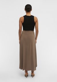 Sort ribbet tanktop parret med en gulvlængde, glat brun nederdel med elastisk talje og en flydende silhuet.