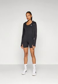 Body desportivo preto com gola redonda e calções justos. Complementado por um casaco leve com fecho éclair e detalhes brancos combinantes.